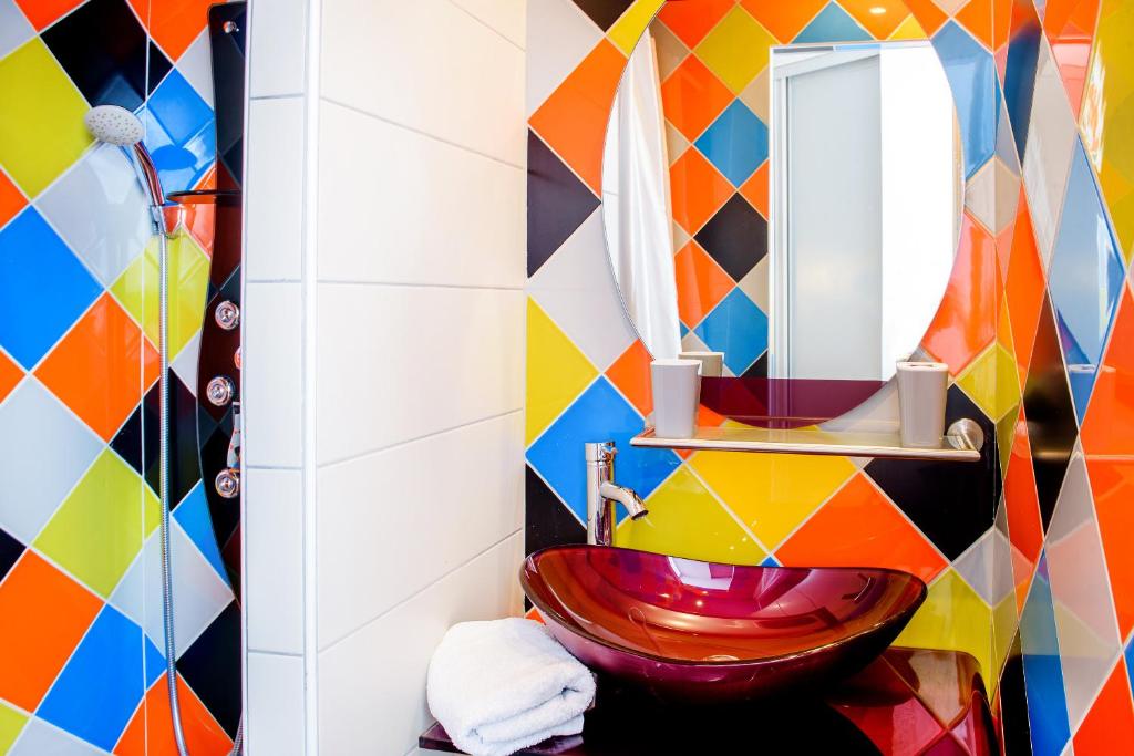 Salle de bain design avec carrelage en losanges multicolores, vasque en verre rouge et miroir rond