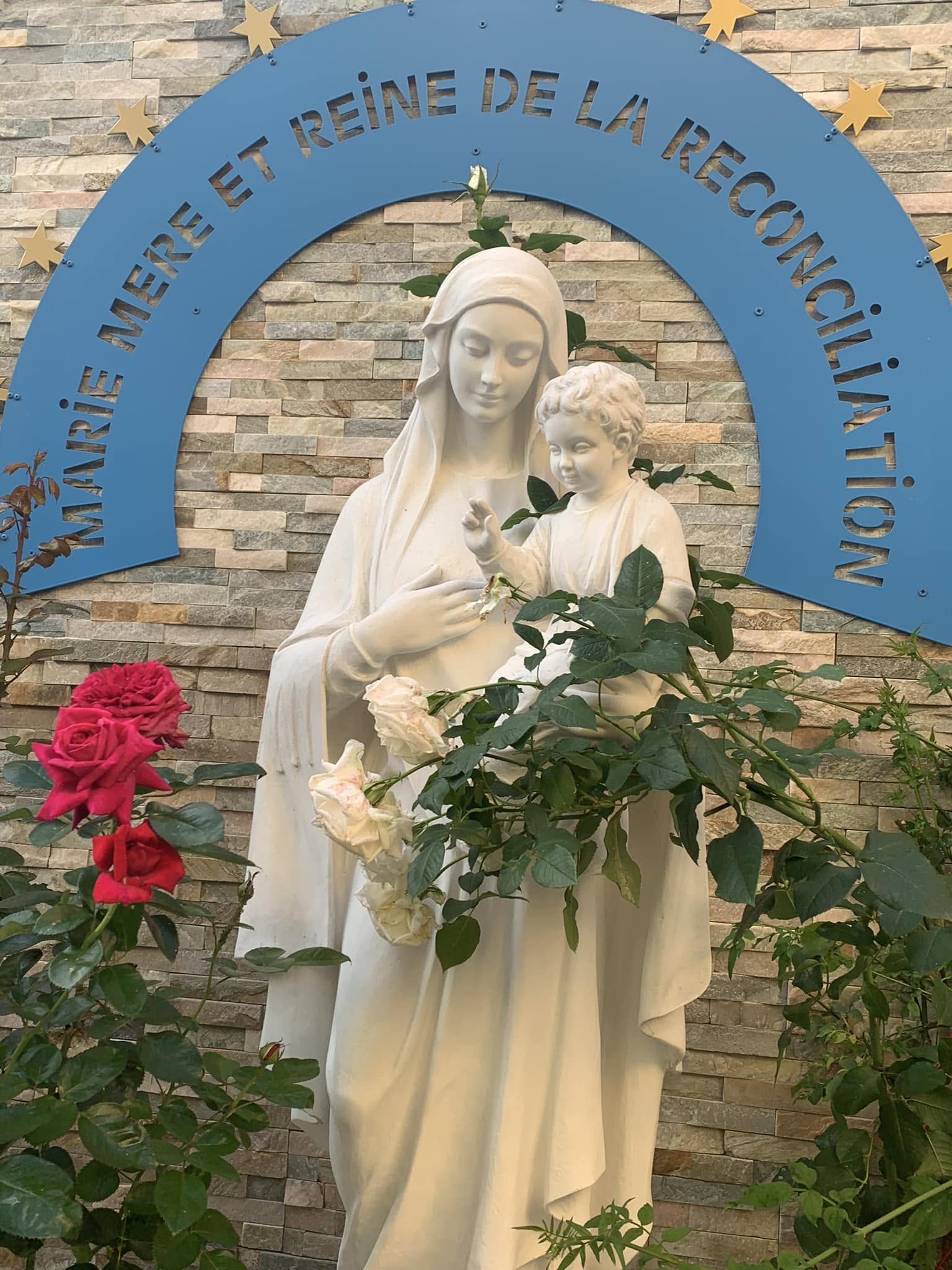 Statue blanche de la Vierge Marie portant l'Enfant Jésus entourée de rosiers