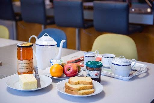 Table de petit-déjeuner garnie d'une théière en porcelaine, de tranches de pain, beurre, confiture, miel et fruits frais.